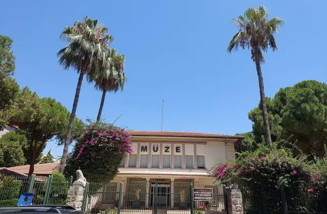 De gevel van het Archeologisch Museum van Alanya tussen palmen en bloeiende bougainville