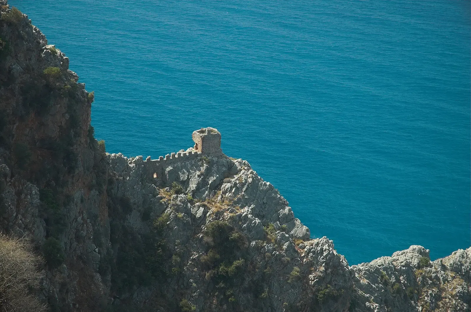 Een wachttoren van de kasteelmuur van Alanya op de rotsen boven turquoise zee